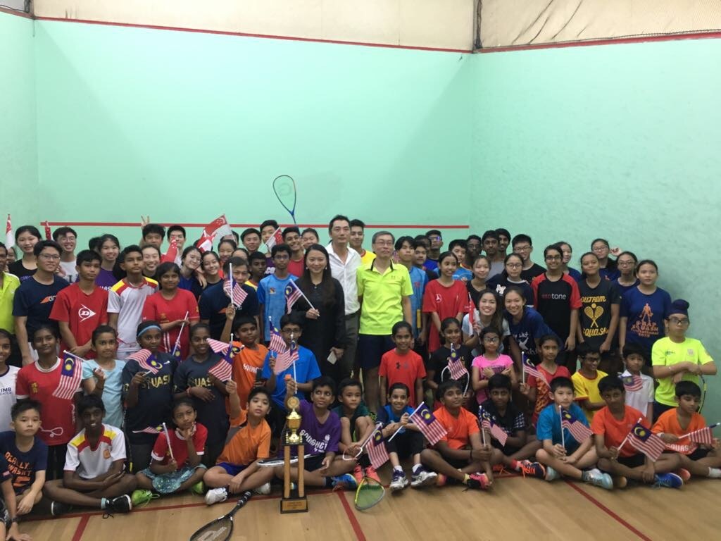 Group of young squash players holding flags with a trophy